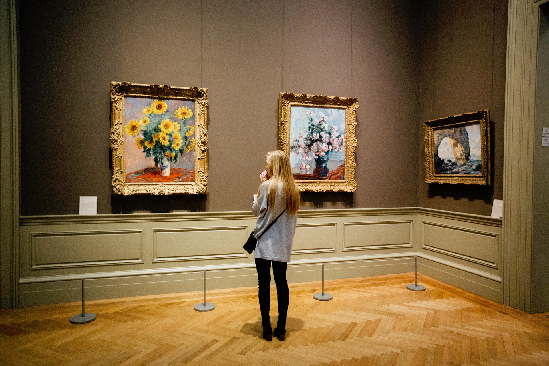 في الصورة امرأة تنظر إلى اللوحات في داخل المتحف