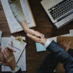 henkilöt kättelevät sopimuspöydän päällä