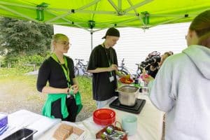 Two people standing outside under a canopy. One is smiling and the other is serving soup onto a plate.