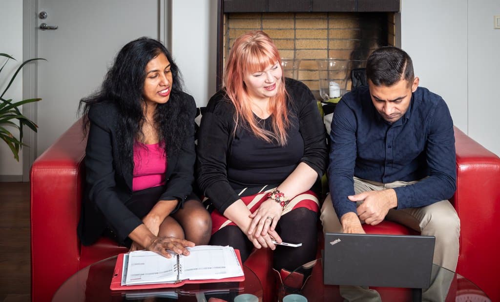 3 people sitting on a sofa and looking at a computer