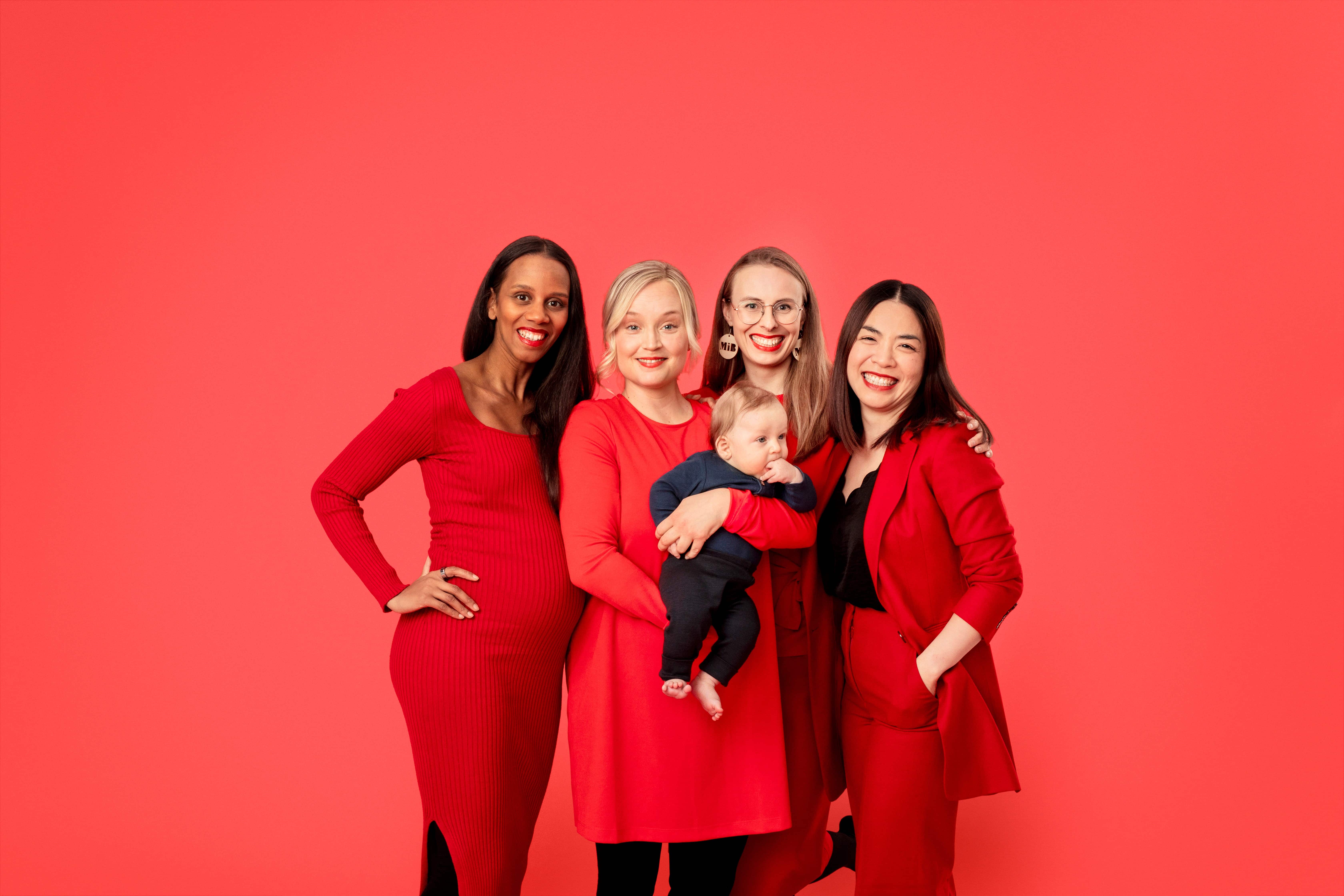 MothersInBusiness Neljä naista poseeraa punaisissa vaatteissa. Yhdellä on vauva sylissä.