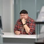 Ihminen istuu pöydän takana ja hymyilee kameralle.