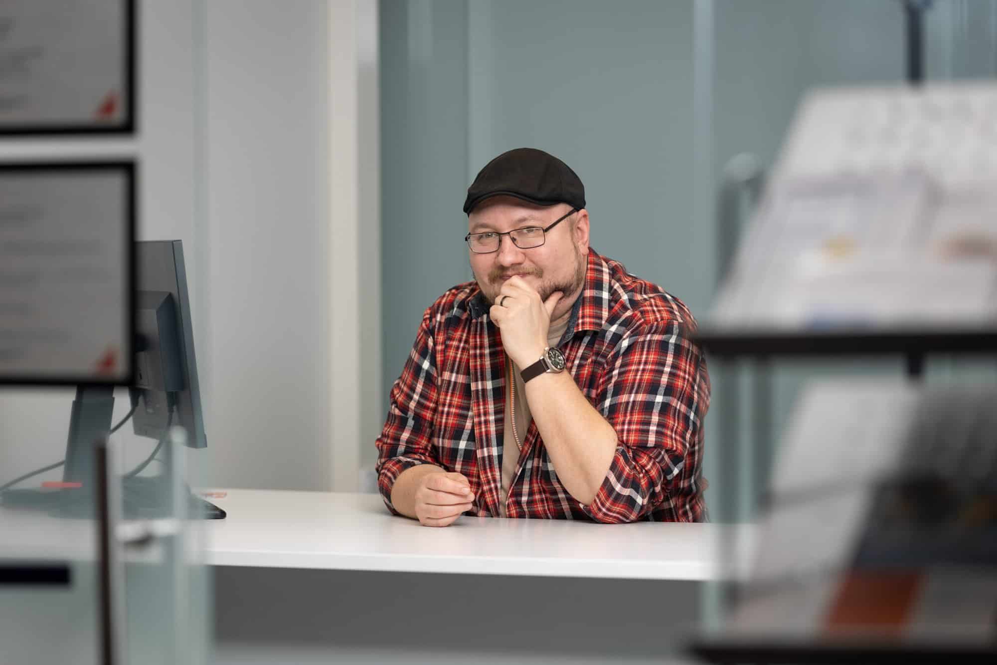 Oksanen Marko-5 (1) Ihminen istuu pöydän takana ja hymyilee kameralle.